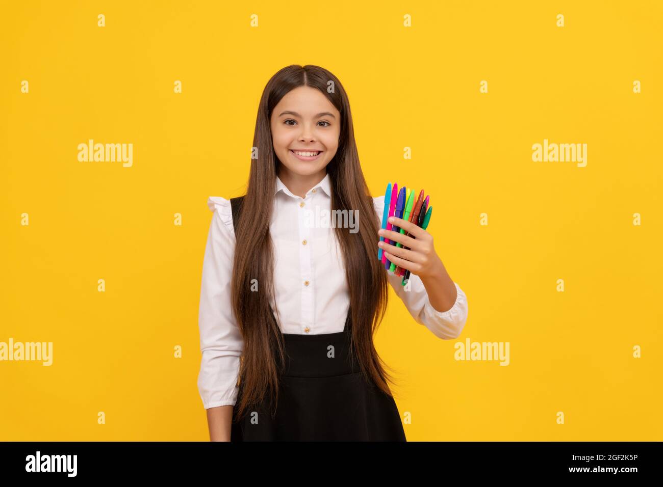 Fille heureuse enfant tenir école papeterie fond jaune, stylos feutre Banque D'Images