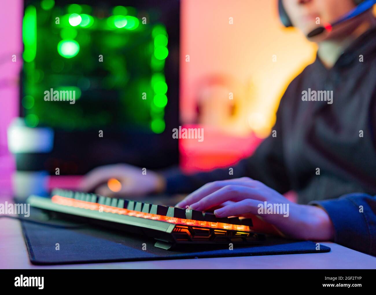 Jeune joueur méconnaissable avec mains sur clavier éclairé dans la pièce avec fond coloré Banque D'Images