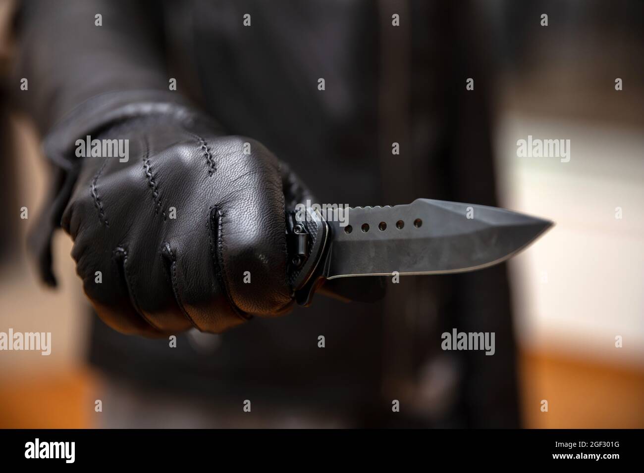 Le voleur menace avec un poignard, un arrière-plan flou, une vue rapprochée. Cambrioleur tenant un couteau dans la main gantée, le concept de cambriolage armé. Banque D'Images