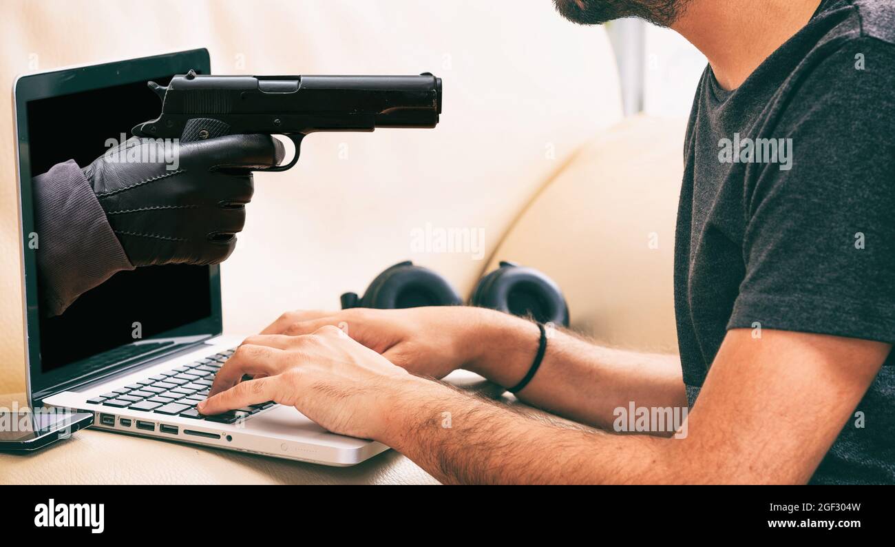 Pistolet et ordinateur portable. Pistolet main gantée destiné au jeune homme travaillant avec un ordinateur. Cybercriminalité, piratage et vol d'informations. Banque D'Images