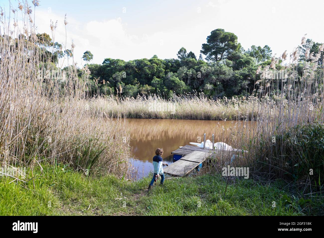 Jeune garçon jouant près d'un lagon sur l'estuaire de la rivière Klein, bateau amarré à un quai Banque D'Images