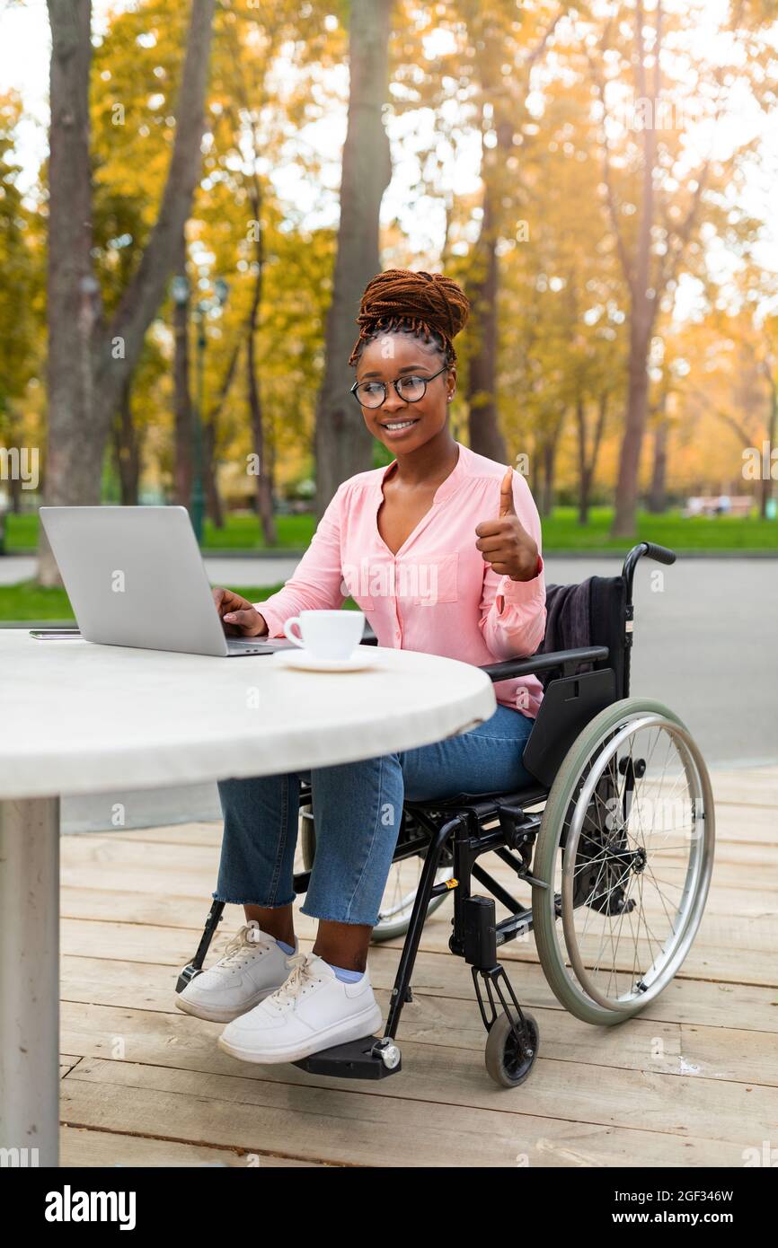 Femme noire handicapée utilisant un ordinateur portable, travaillant en  ligne, montrant le pouce vers le haut au parc d'automne. Travail à distance  pour les personnes handicapées Photo Stock - Alamy