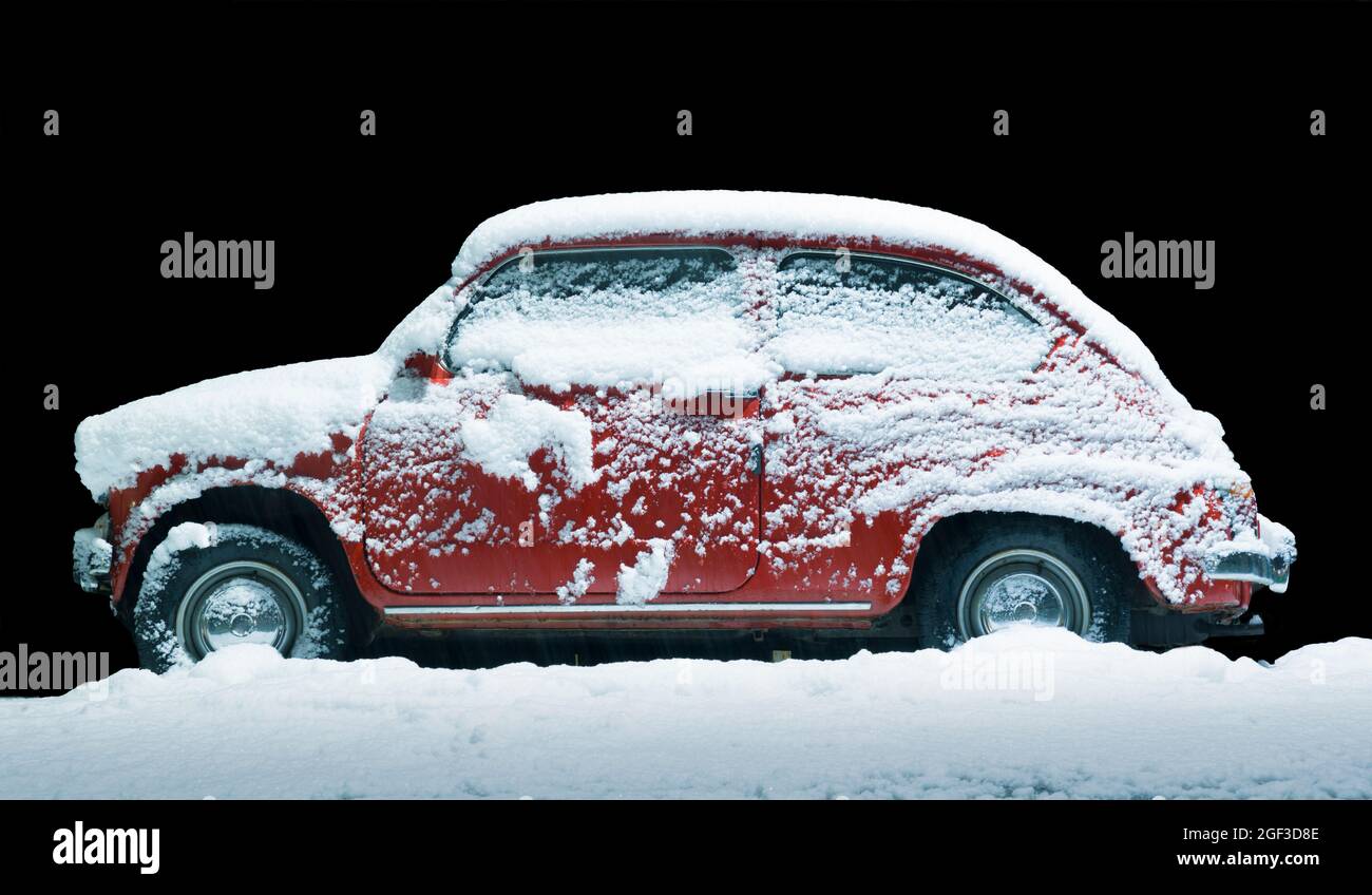 Petite vieille voiture rouge couverte de neige la nuit Banque D'Images