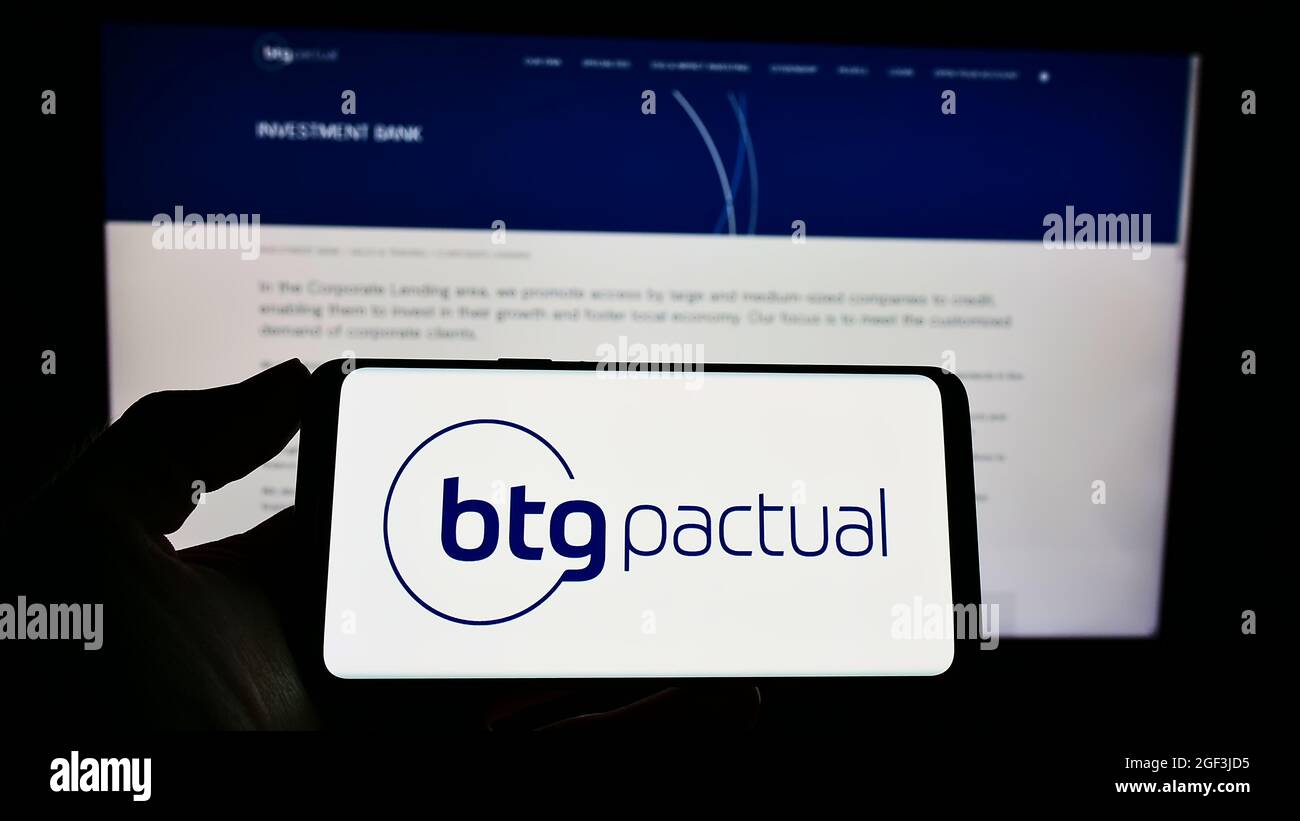 Personne tenant un téléphone portable avec le logo de la société financière brésilienne BTG Penal sa à l'écran en face de la page Web d'affaires. Mise au point sur l'affichage du téléphone. Banque D'Images