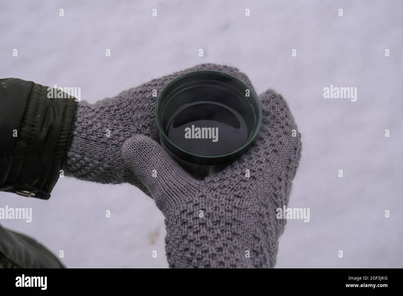 mains dans des gants tricotés chauds tenant une boisson chaude dans une tasse thermo vue du dessus de la surface enneigée. Trekking en hiver. Copier l'espace Banque D'Images