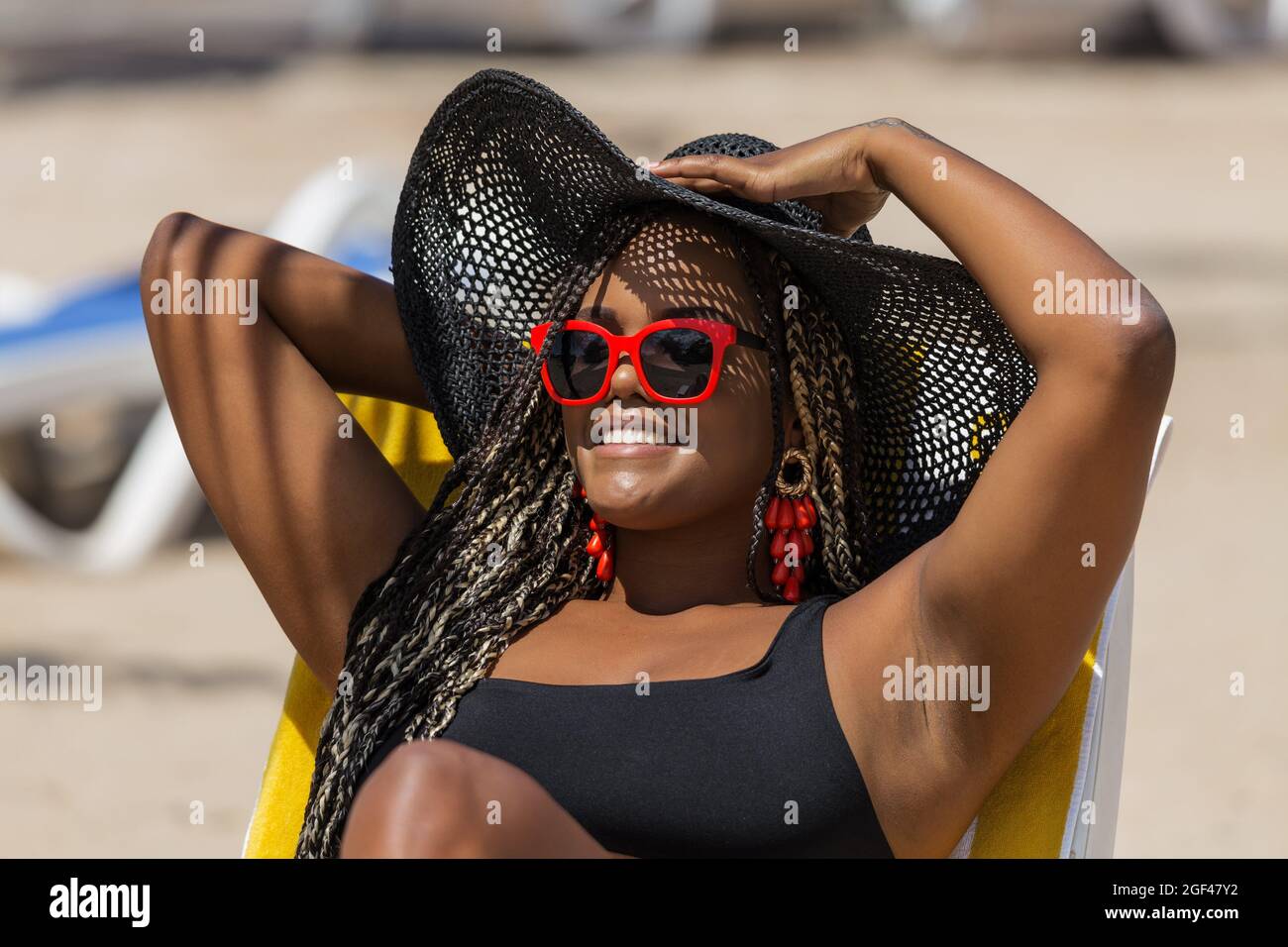 Gros plan d'une femme afro-américaine sur la plage, allongé sur une chaise  longue portant un chapeau noir et des lunettes de soleil. Femme adulte  joyeuse appréciant un été Photo Stock - Alamy
