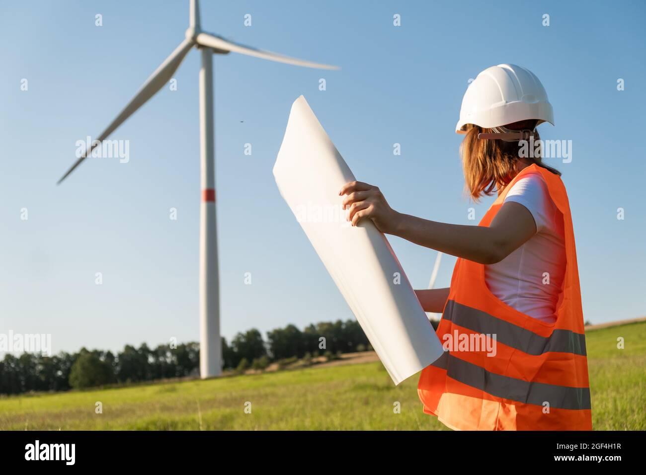 Un ingénieur des éoliennes tenant un projet papier et regardant le moulin à vent sur le terrain. Production écologique d'électricité et d'énergie renouvelable. Banque D'Images