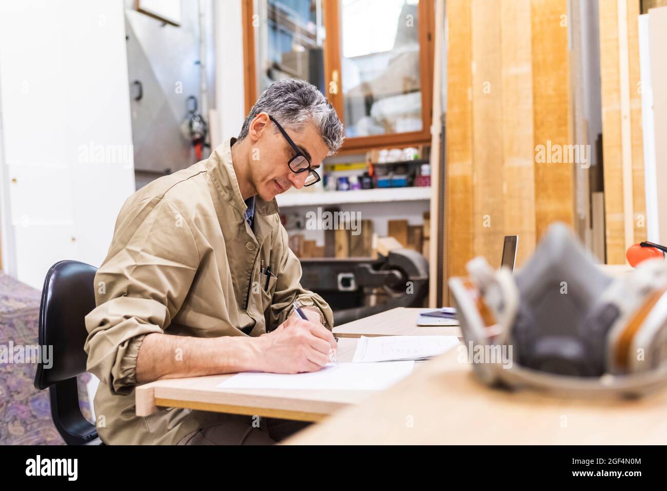 Menuisier mâle mûr écrivant sur papier à la table en atelier Banque D'Images