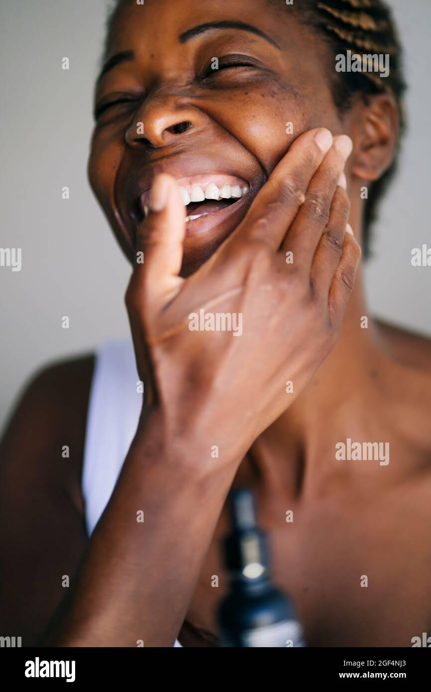 Femme afro souriant tout en touchant le visage Banque D'Images