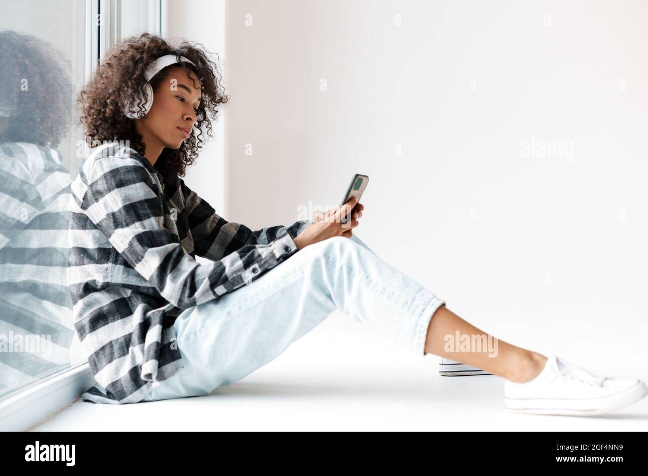 Femme africaine dans un casque utilisant un téléphone portable tout en étant assis à l'intérieur de la fenêtre Banque D'Images