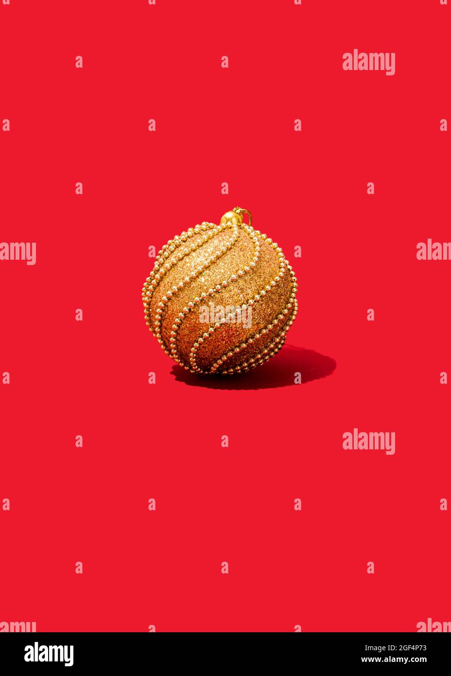 Photo de studio d'un seul ornement de Noël doré sur fond rouge vif Banque D'Images
