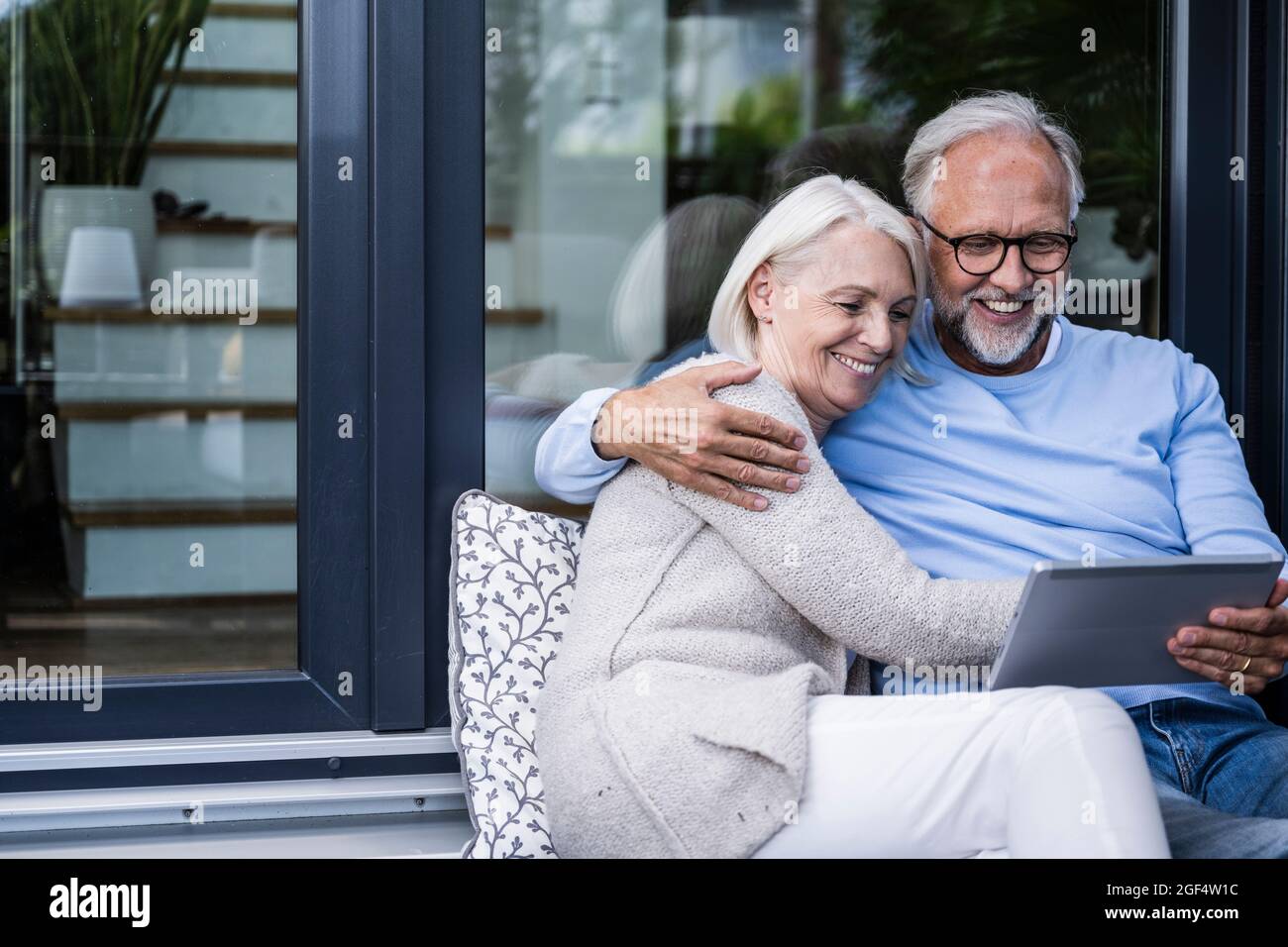 Homme souriant utilisant une tablette numérique tout en étant assis avec le bras autour de la femme sur le balcon Banque D'Images