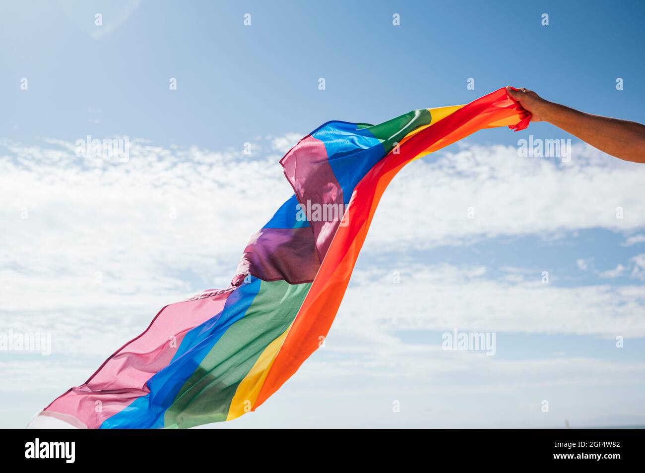 Un homme gay heureux se faisant le geste tout en agitant le drapeau de l'arc-en-ciel pendant la journée ensoleillée Banque D'Images