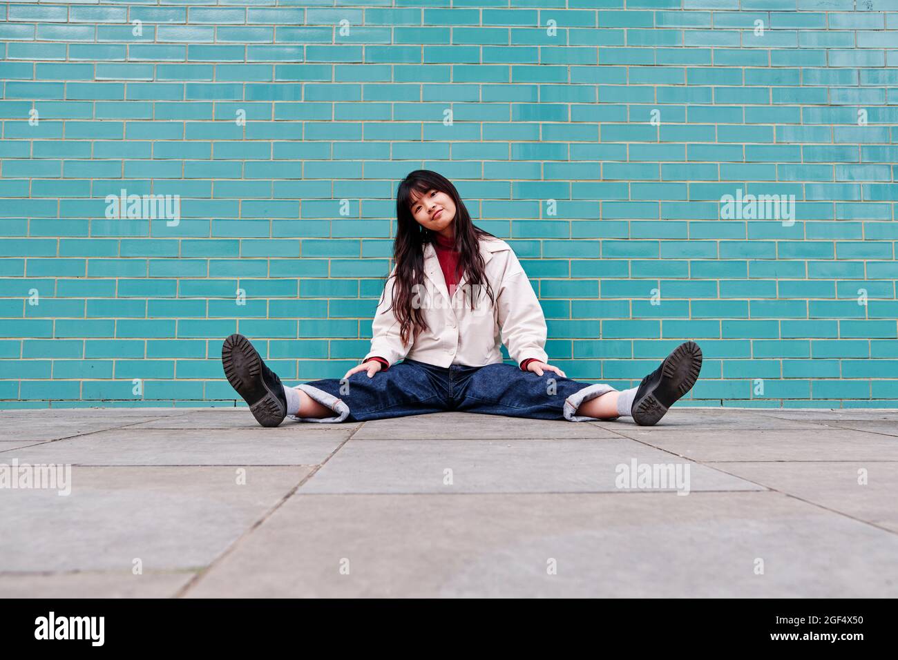 Belle jeune femme assise avec les jambes à part devant le mur de brique Banque D'Images