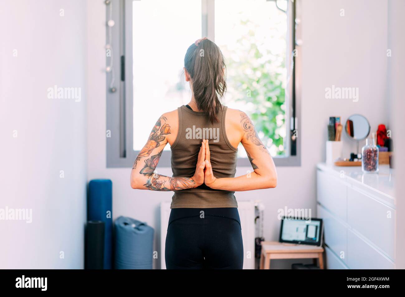 Femme aux mains clastées derrière le dos pratiquant le yoga à la maison Banque D'Images