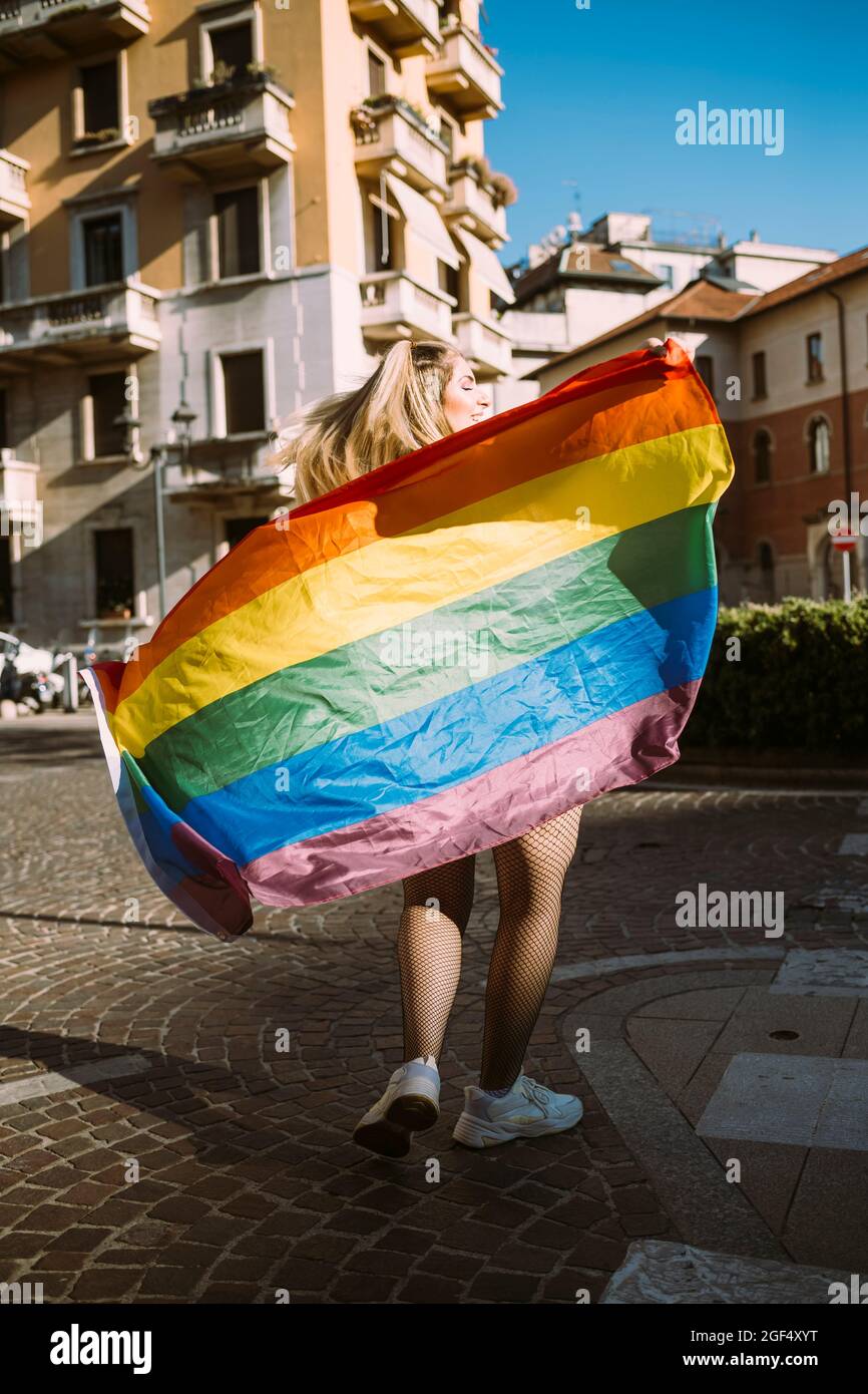 Jeune militante avec drapeau arc-en-ciel marchant dans la rue pendant la journée ensoleillée Banque D'Images
