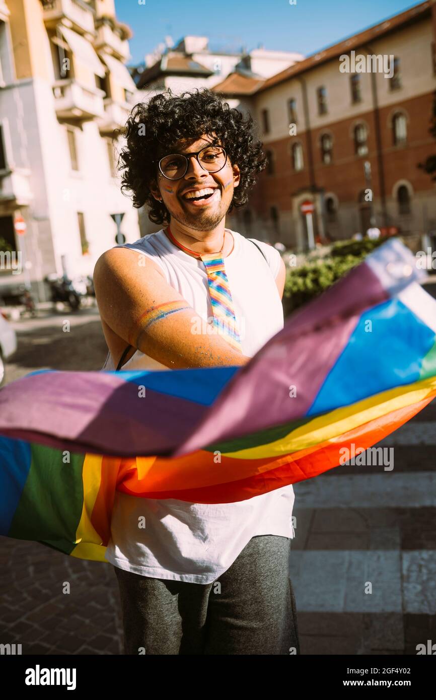 Joyeux manifestant masculin avec drapeau arc-en-ciel dans la rue Banque D'Images