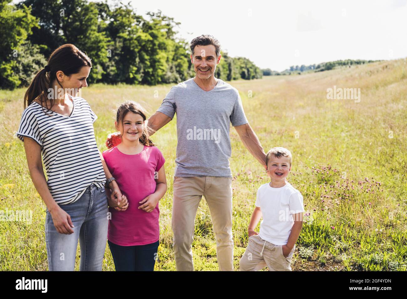 Parents souriants debout avec des enfants dans la prairie pendant la journée ensoleillée Banque D'Images