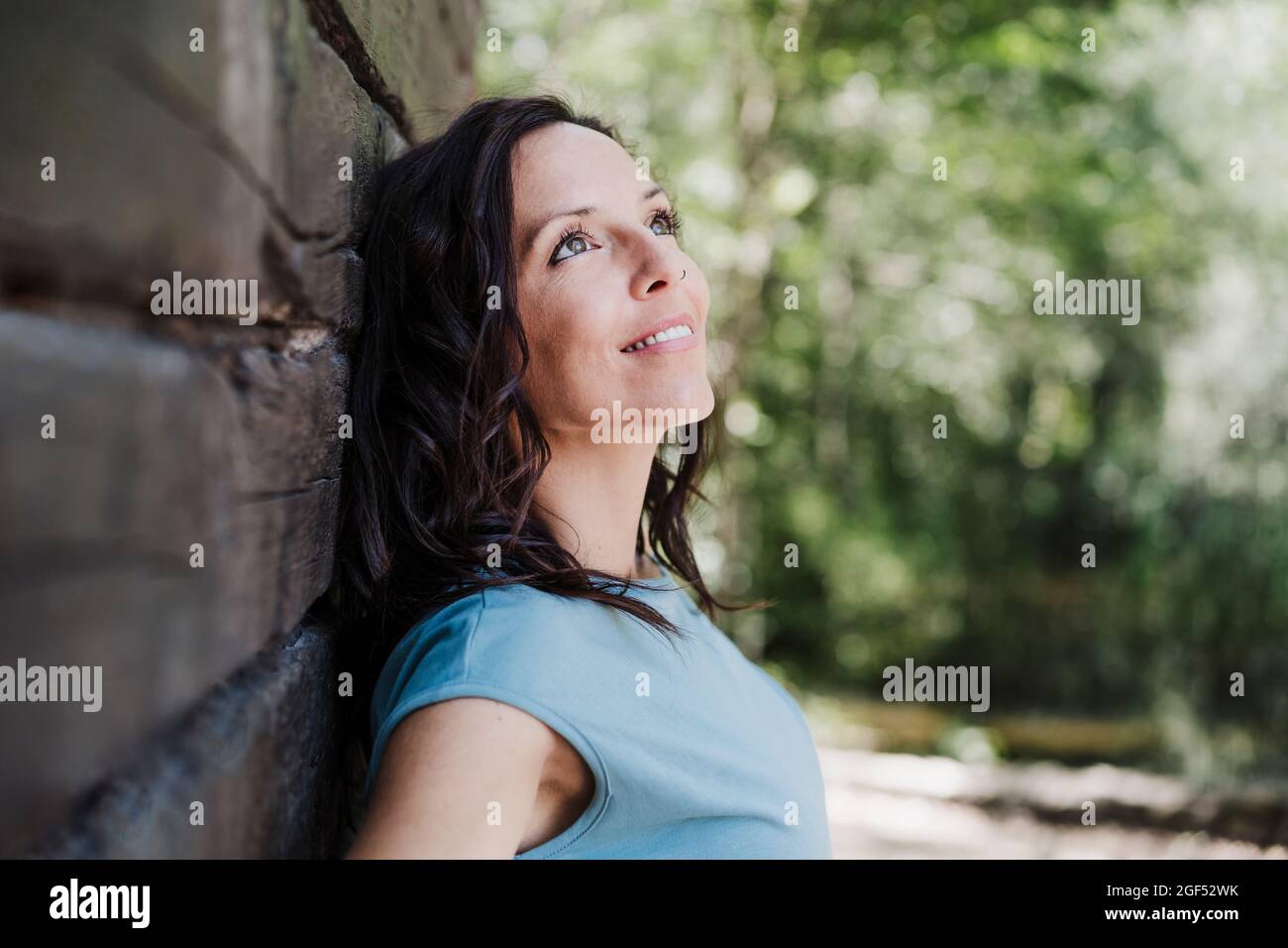 Souriante femme adulte de taille moyenne regardant loin tout en s'appuyant sur le mur Banque D'Images