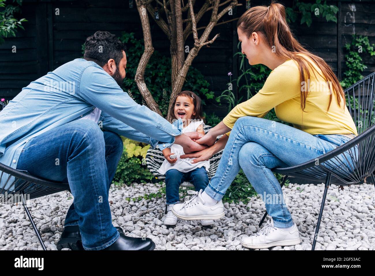 Parents avec les mains empilées assis par fille joyeuse à la cour arrière Banque D'Images