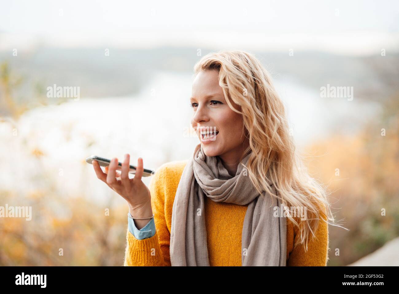 Femme blonde envoyant la messagerie vocale par smartphone pendant l'automne Banque D'Images