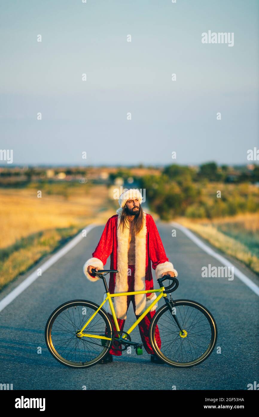 Homme en costume du Père Noël debout avec vélo sur la route Banque D'Images