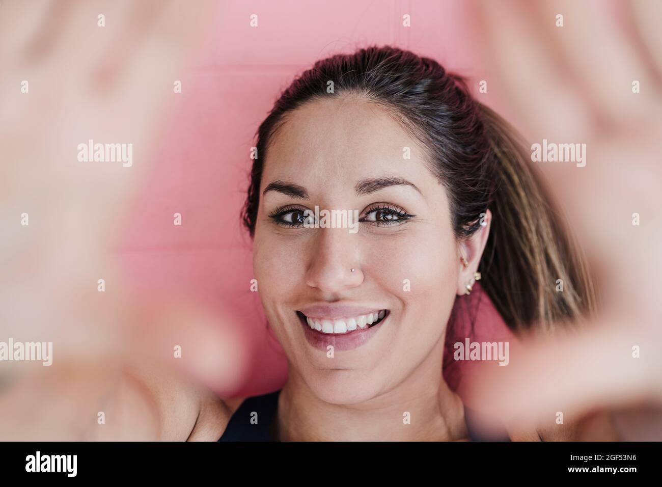 Une athlète féminine souriante se fait un corps de doigt tout en étant allongé sur un tapis d'exercice Banque D'Images