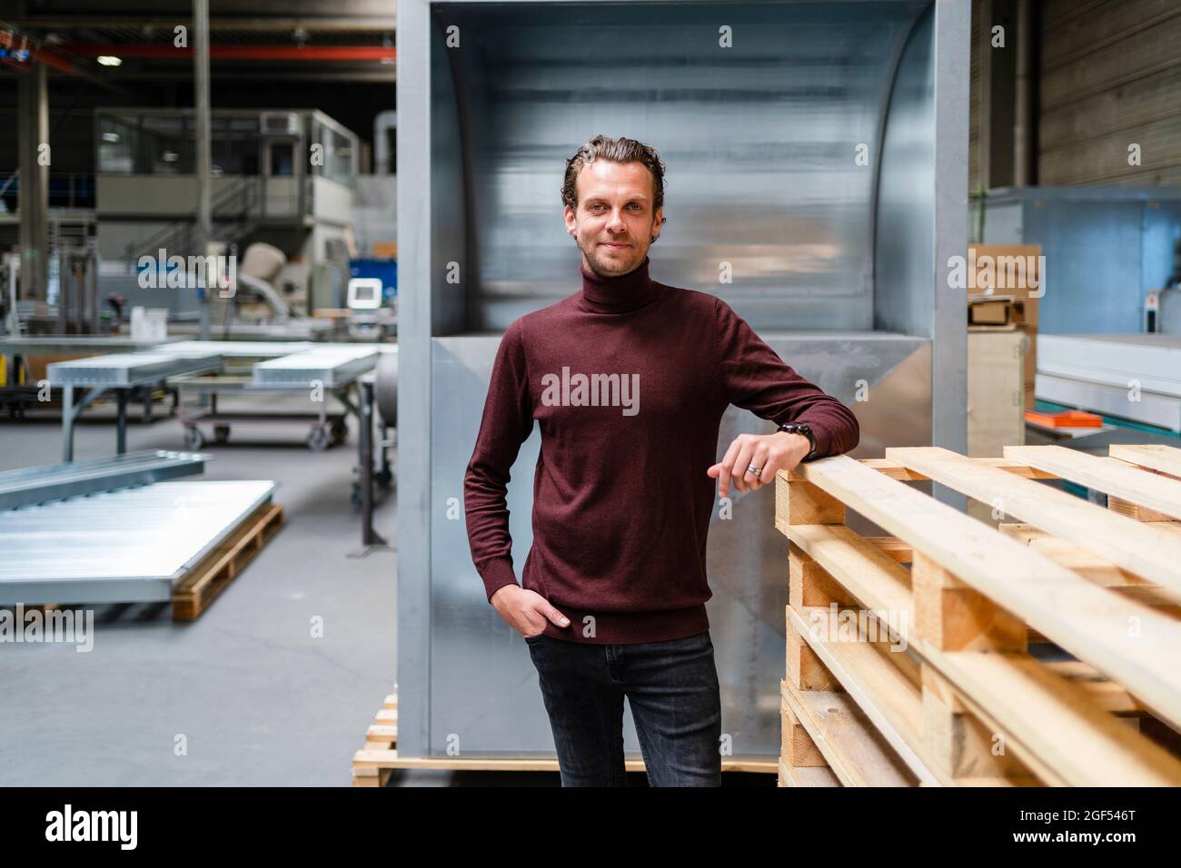 Homme professionnel avec main dans la poche debout par pile de palettes en bois Banque D'Images