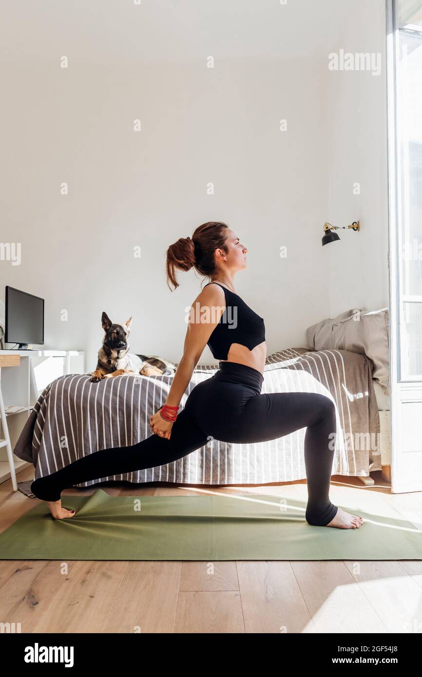 Femme flexible s'étirant tout en pratiquant le yoga dans l'appartement Banque D'Images