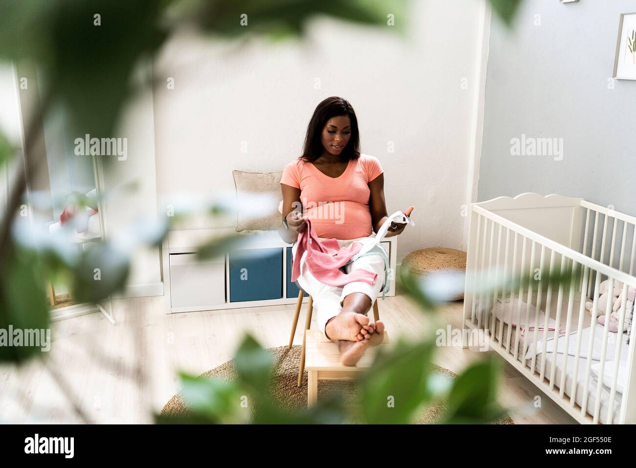 Femme enceinte assise avec des vêtements pour bébé sur une chaise dans la chambre Banque D'Images