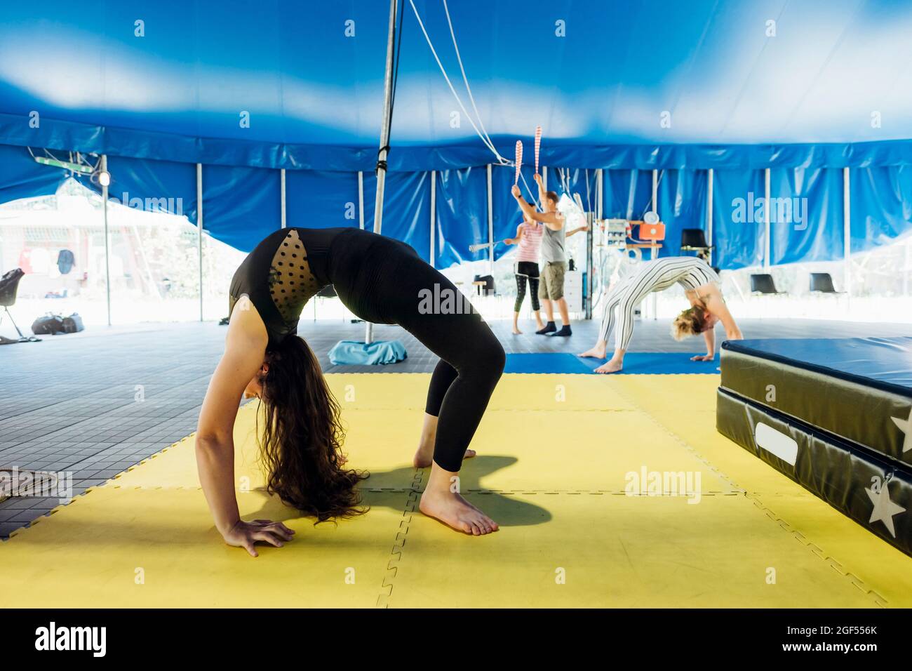 Une artiste féminine se repliant vers l'arrière tout en s'exerçant avec des athlètes en arrière-plan au cirque Banque D'Images