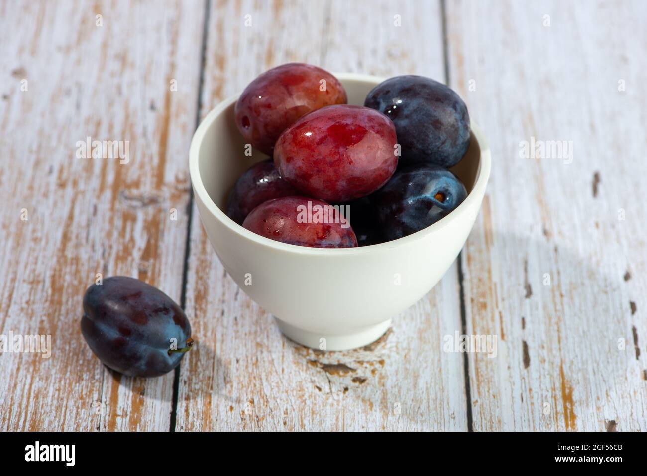 Fruits prune frais dans un bol blanc sur une table en bois. Banque D'Images