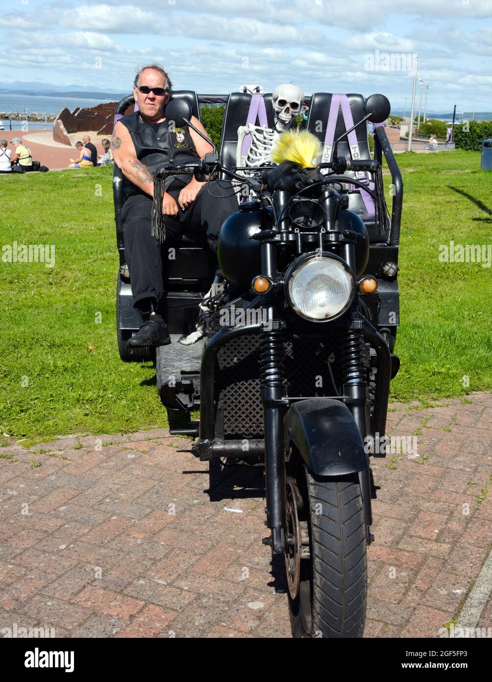 Un homme est assis dans une moto à trois roues avec un faux squelette à la station balnéaire de Morecambe, Lancashire, Angleterre, Royaume-Uni. Banque D'Images