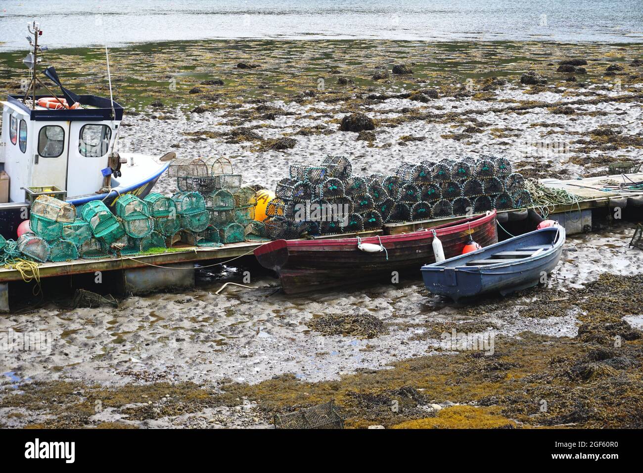 Des bateaux de pêche ont été pêchés sur des plates-clés à marée basse, à côté d'un quai entassé de pots de homard et de crevettes au village de Plockton, en Écosse Banque D'Images