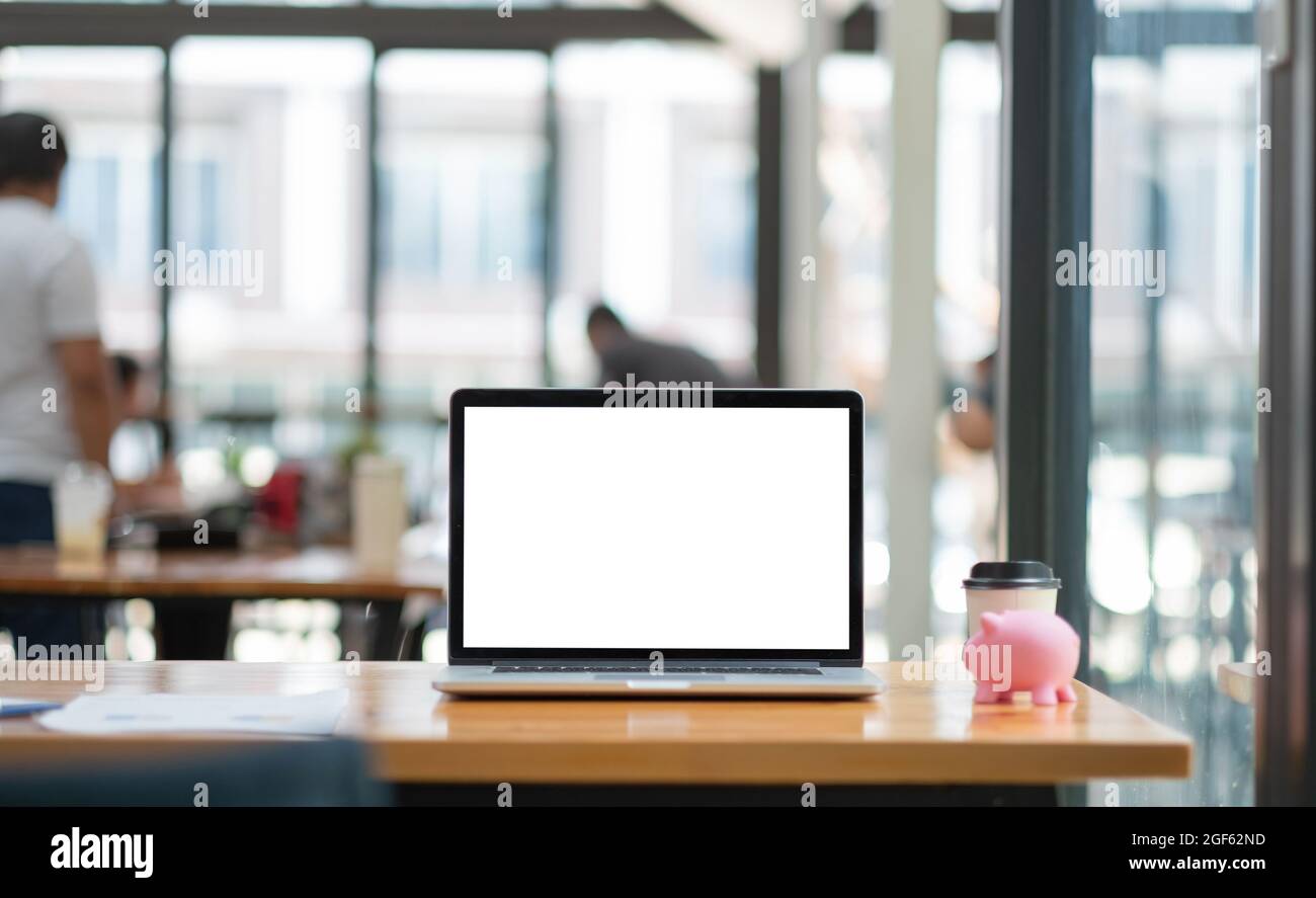 Ordinateur portable avec écran blanc sur le bureau de travail, économie d'argent avec la banque de porc rose. Banque D'Images