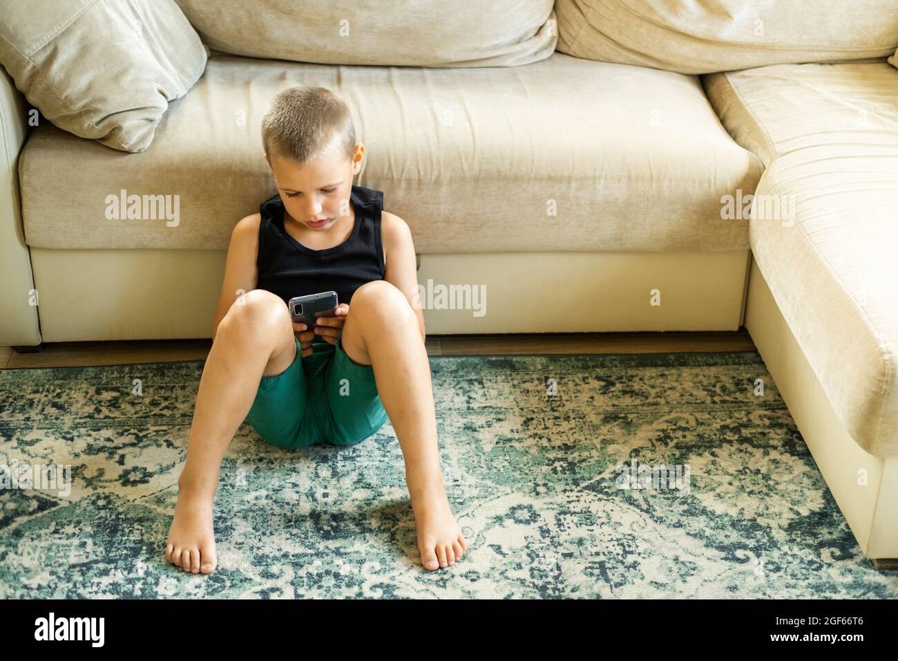 Jeune garçon assis sur le sol et jouant ou regardant la vidéo dans un smartphone. Communication Internet, technologies modernes et concept de personnes. Banque D'Images