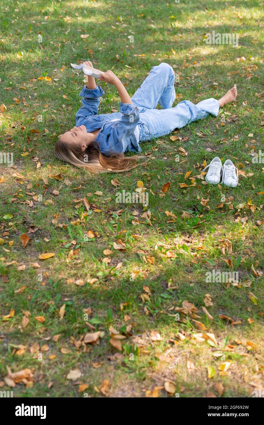Photo d'une femme lisant un livre dans le parc. Elle prend une pause de travailler à l'ordinateur et constamment en ligne. Concept de détox numérique. Banque D'Images