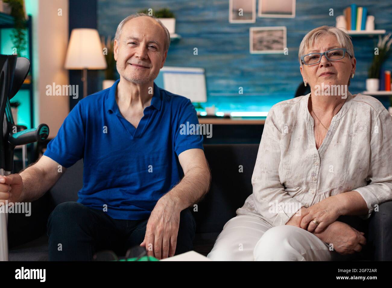 Portrait d'un couple âgé assis ensemble à la maison dans un salon décoré. Un vieux mari caucasien avec une béquille de transport pour personnes handicapées et une femme âgée souriant regardant la caméra Banque D'Images
