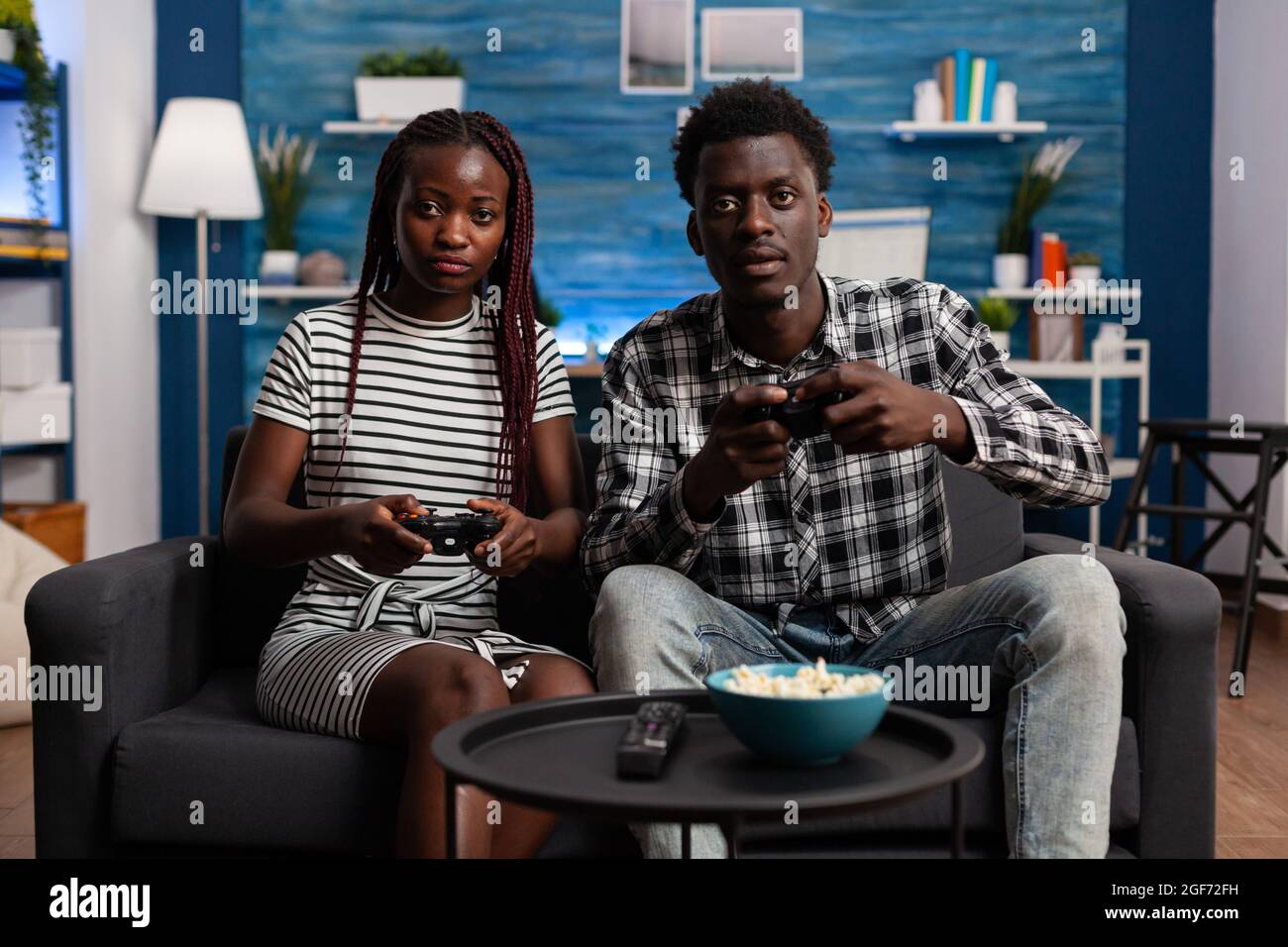 Couple afro-américain jouant à un jeu vidéo sur une console de télévision en utilisant des contrôleurs à l'écran de télévision dans le salon. Les personnes mariées noires profitent d'activités modernes pour s'amuser et se divertir Banque D'Images