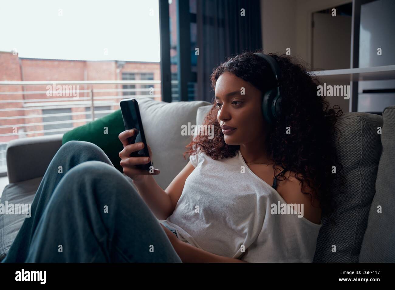 Course mixte femme adolescent textant sur un appareil cellulaire se reposant sur un canapé Banque D'Images