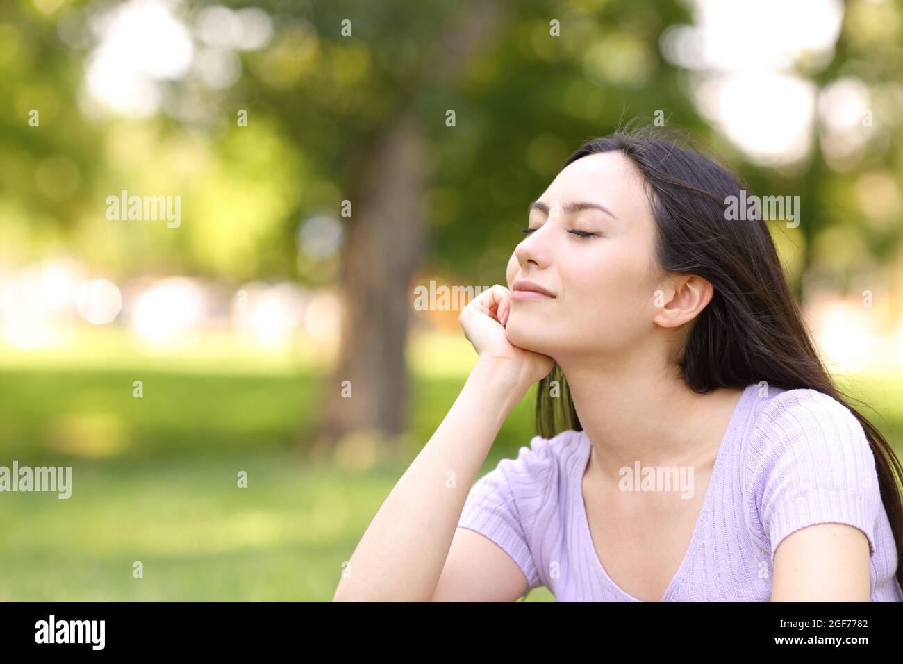 Femme asiatique satisfaite se reposant avec les yeux fermés dans un parc Banque D'Images