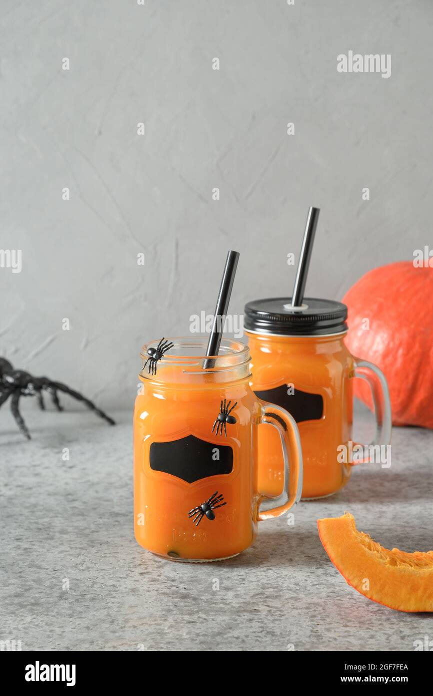 Cocktails d'Halloween avec jus de citrouille, épices, araignées de garniture pour la fête sur fond gris avec toile d'araignée d'horreur. Gros plan. Format vertical. Banque D'Images