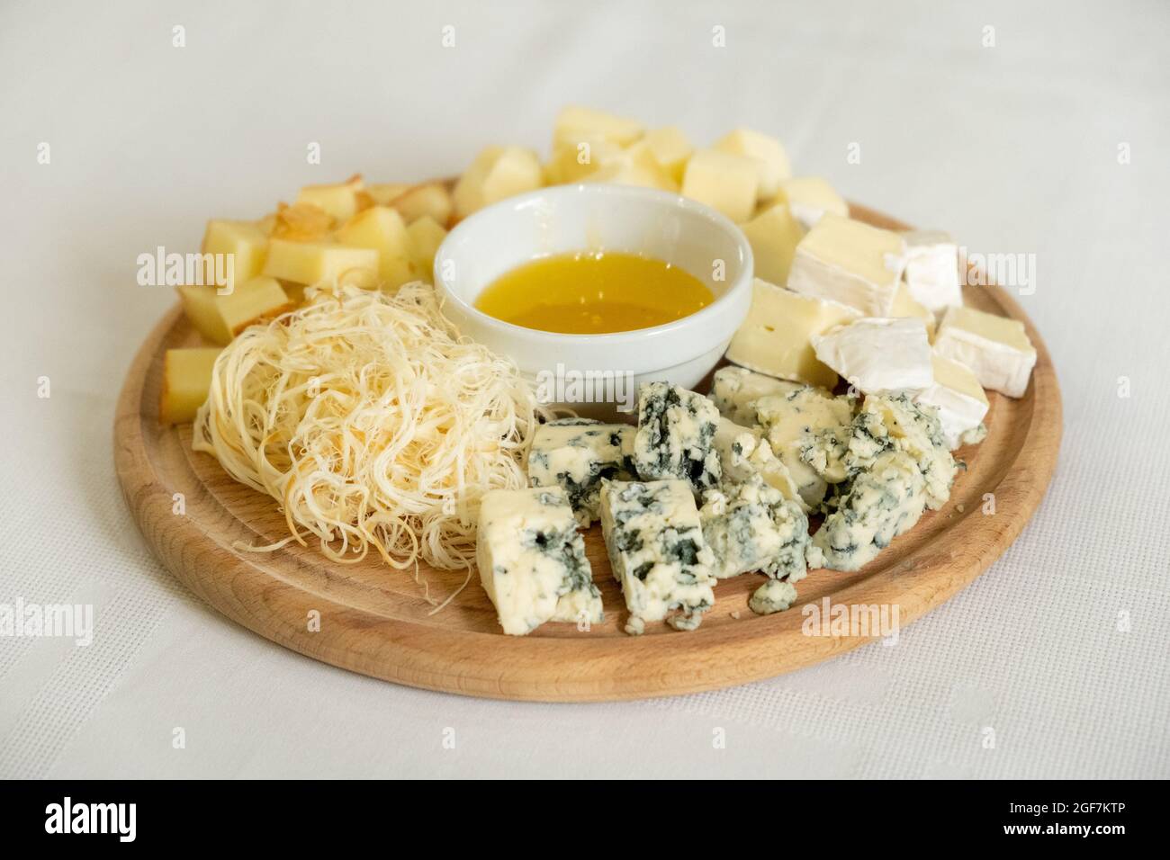 Planche en bois avec divers types de fromages et bol de miel, en-cas sain, concentration sélective Banque D'Images