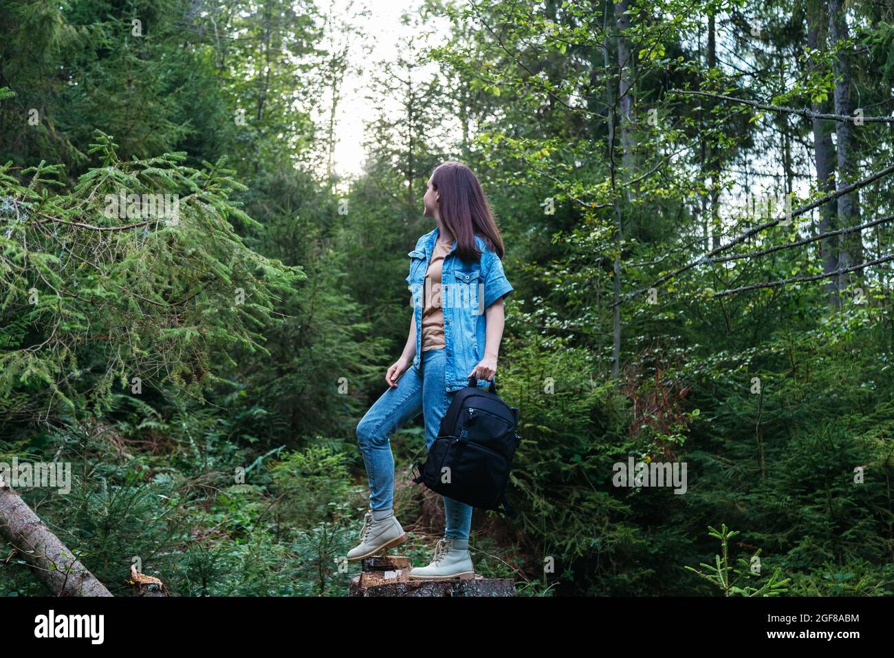 Femme en costume denim en bottes avec sac à dos photo est engagée dans la randonnée en forêt. Jeune femme caucasienne méconnaissable marchant dans la nature dans le parc Banque D'Images