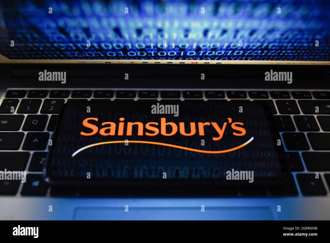 Portugal. 24 août 2021. Sur cette photo, un logo de Sainsbury apparaît sur un smartphone avec code binaire sur un écran d'ordinateur portable. Crédit : SOPA Images Limited/Alamy Live News Banque D'Images