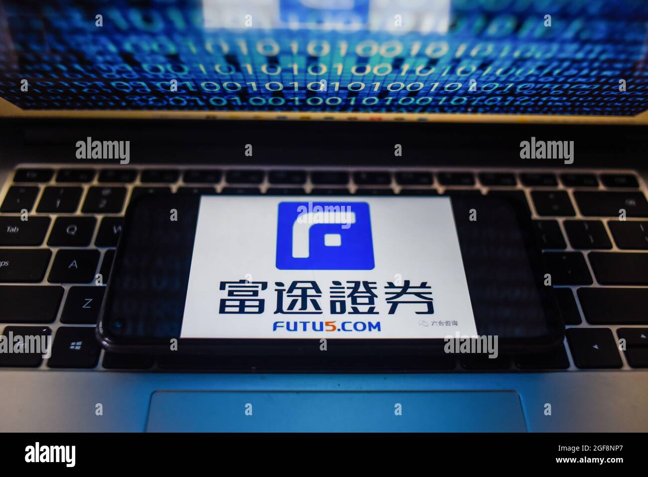 Portugal. 24 août 2021. Sur cette photo, un logo Futu Holdings apparaît sur un smartphone avec un code binaire sur un écran d'ordinateur portable. Crédit : SOPA Images Limited/Alamy Live News Banque D'Images