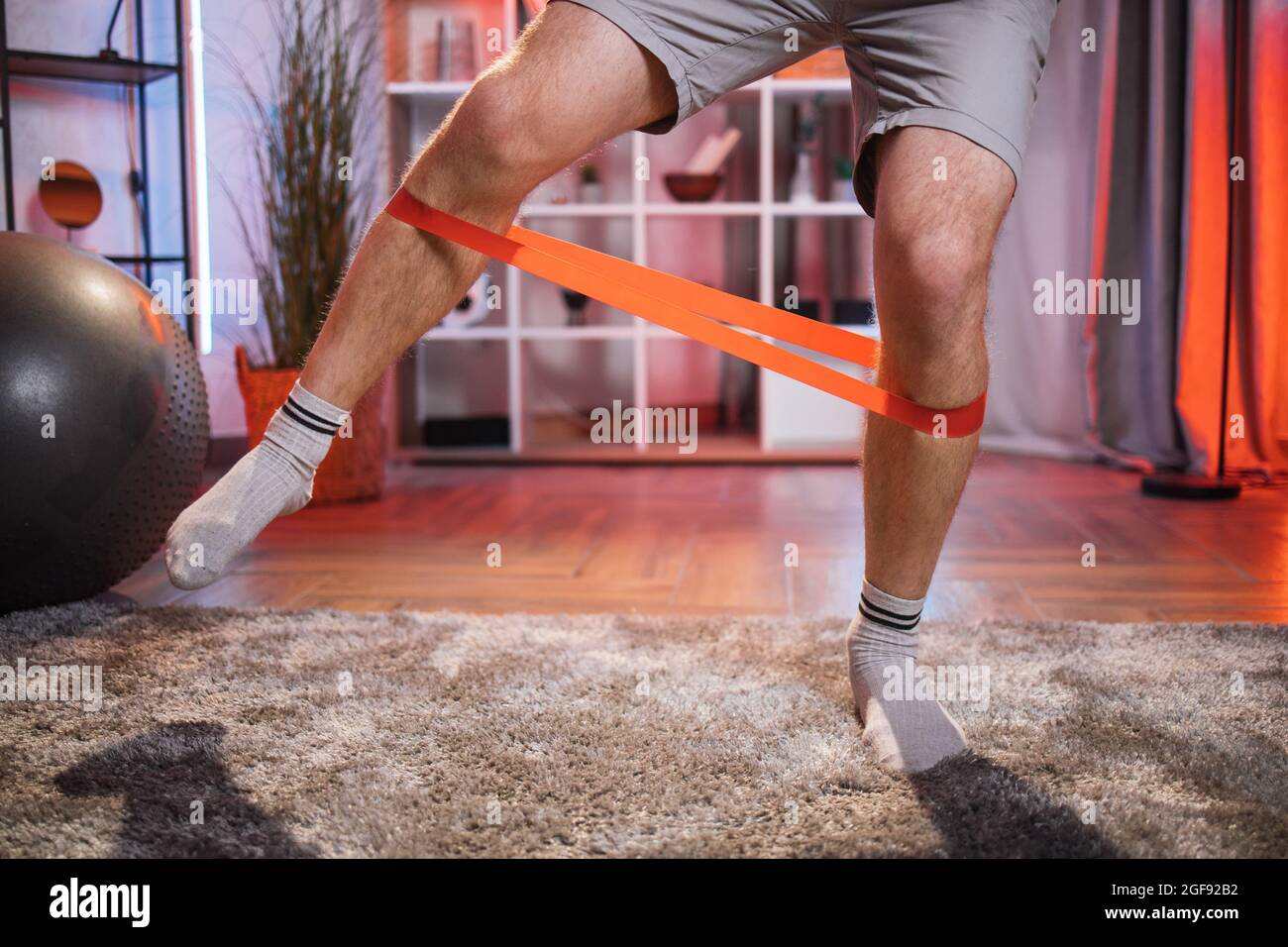 Gros plan de l'homme en short et chaussettes avec bande de résistance pour l'entraînement  des jambes à la maison. Homme faisant des exercices de remise en forme avec  des équipements de sport.