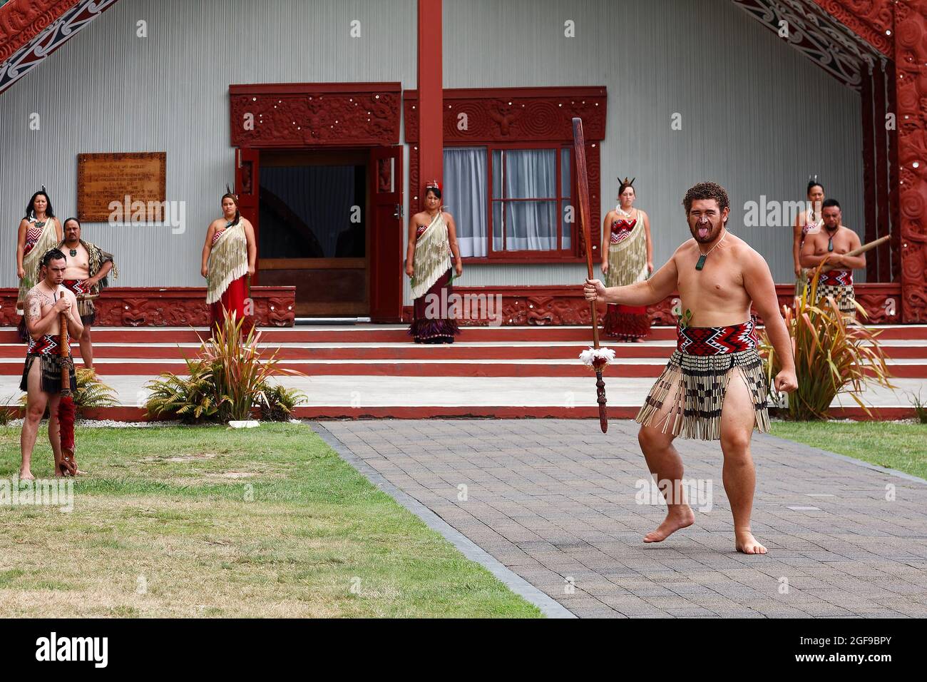 Les Maoris exécutant la cérémonie d'accueil du chef, bâtiment extérieur, homme dansant, langue dehors, autres regardant, Robe indigène, indigène, te Puia Maori Banque D'Images