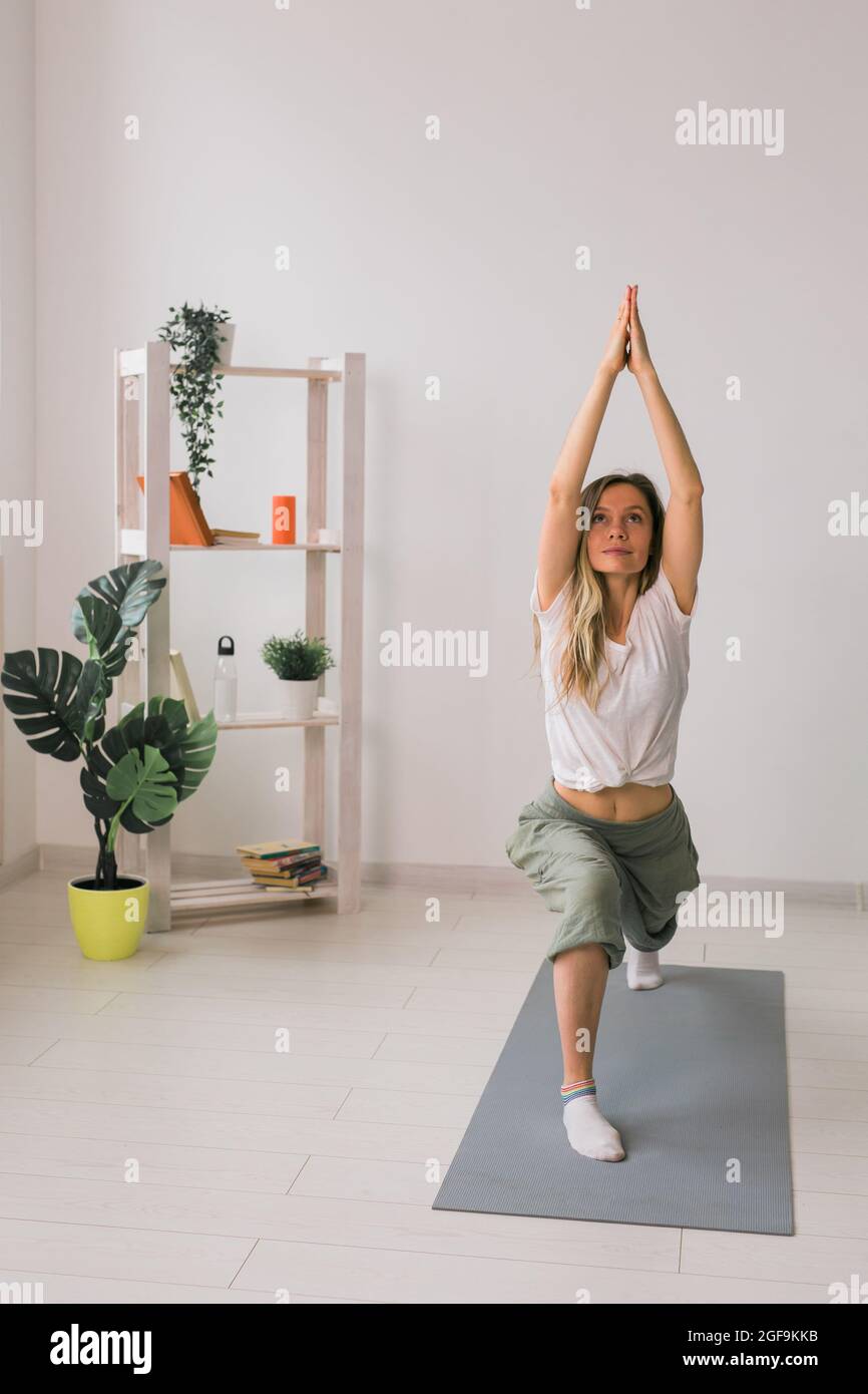 Une femme pratique des cours de yoga. Posez sur le tapis à l'intérieur d'une pièce confortable avec des plantes et de la verdure. Concept de mode de vie sain. Banque D'Images