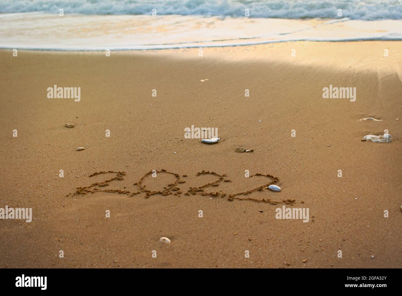 2022 bonne inscription du nouvel an plage de sable. Le texte écrit est écrit sur du sable jaune et est lavé par une vague. Le concept de changer l'année, Banque D'Images